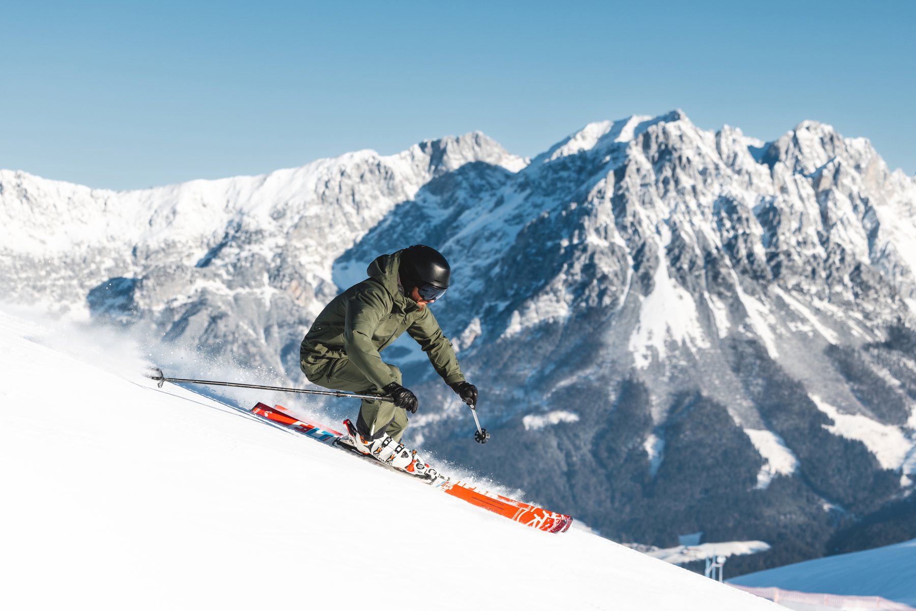 Jack Chamberlain carving a turn at speed with the Wilder Kaiser massif behind him.
