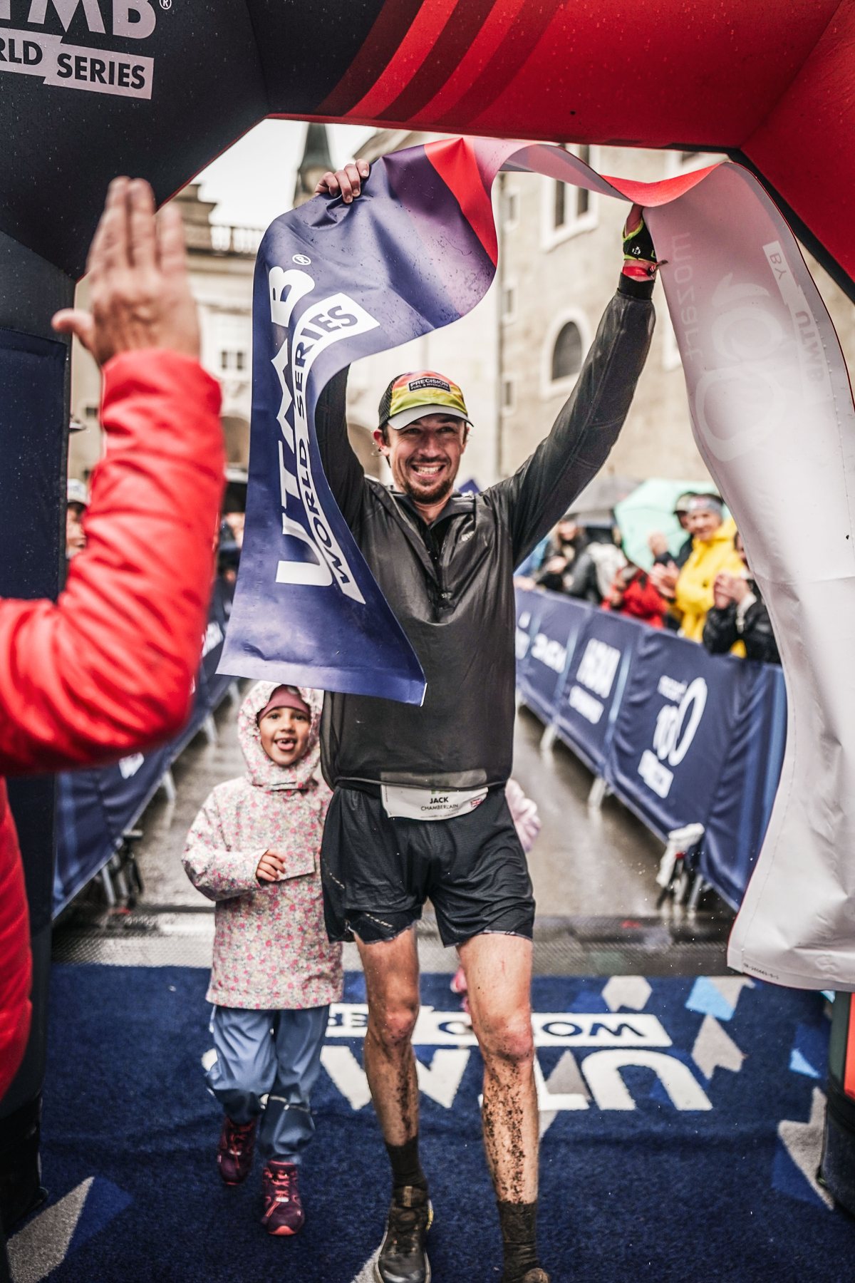 Jack Chamberlain holding the finish banner above his head after winning the Mozart 100 in Salzburg, his daughter beside him.